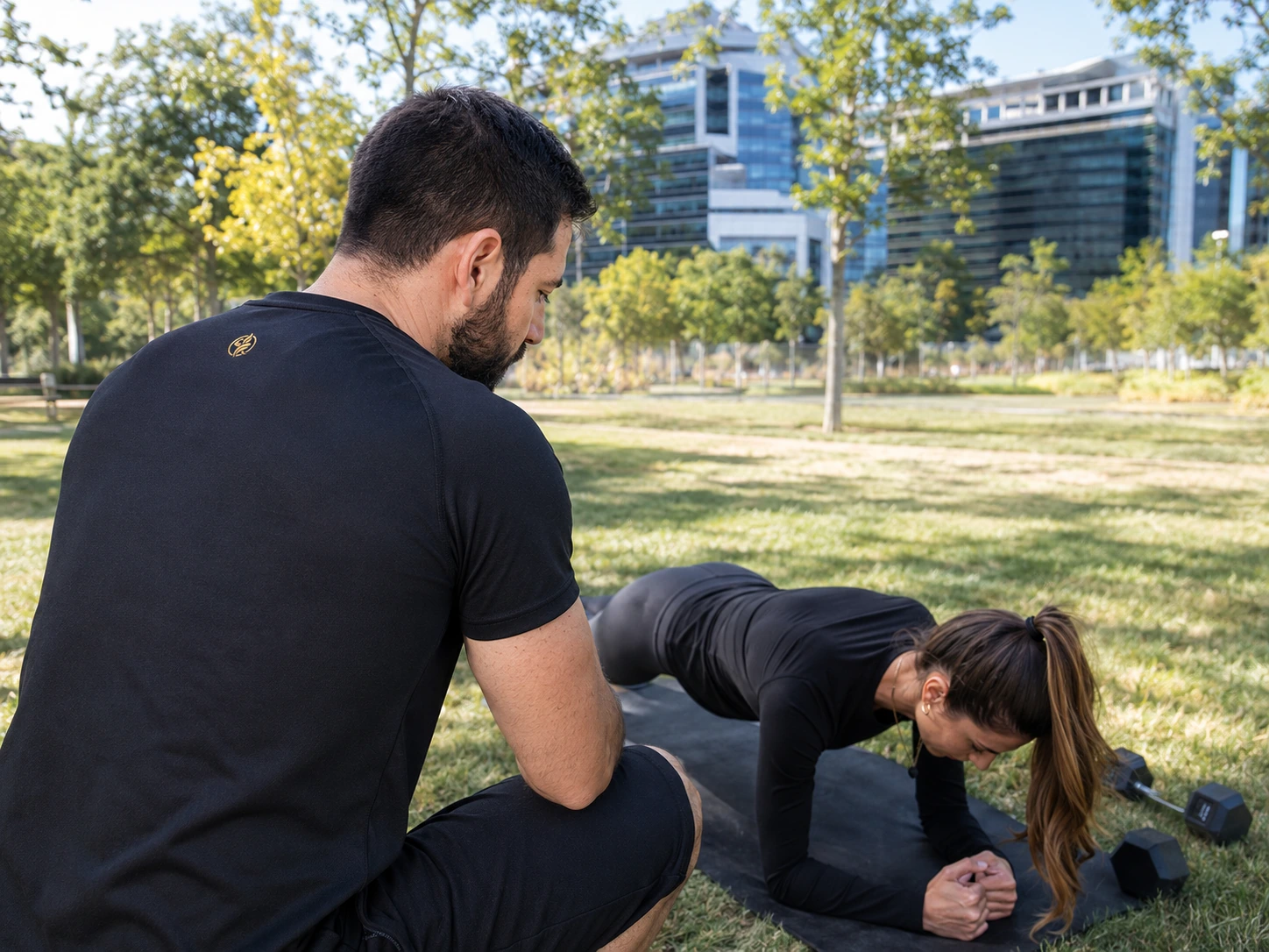 Entrenador IBERFIT supervisando una sesión de entrenamiento personal al aire libre.